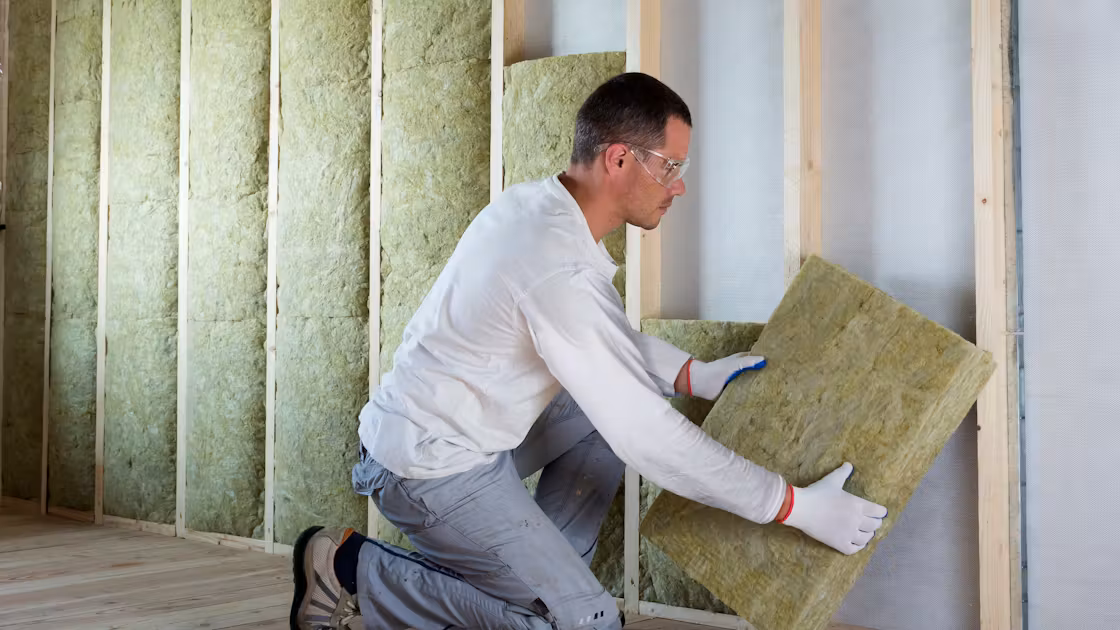 An installer fitting a Rockwool slab between timber studs