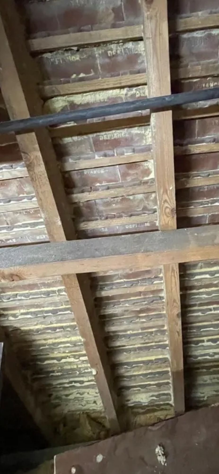 A close view of roof rafters and tile battens under clay tiles, with traces of yellow spray foam left between the battens