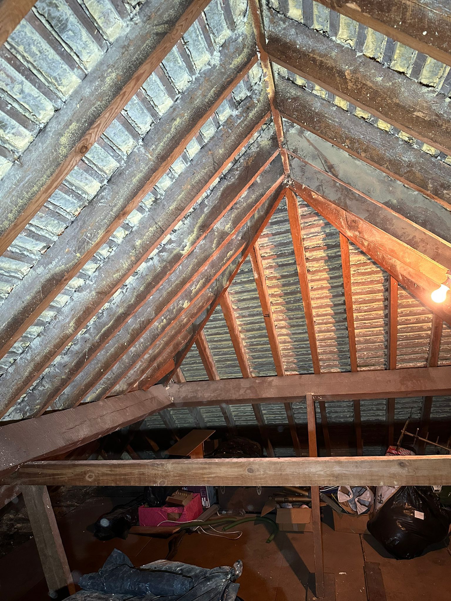A pitched loft roof cleared of spray foam, its rafters and tile battens on show